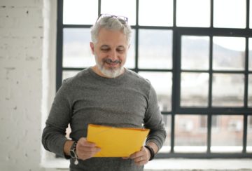 cheerful-mature-male-employee-holding-documents-against-3931608